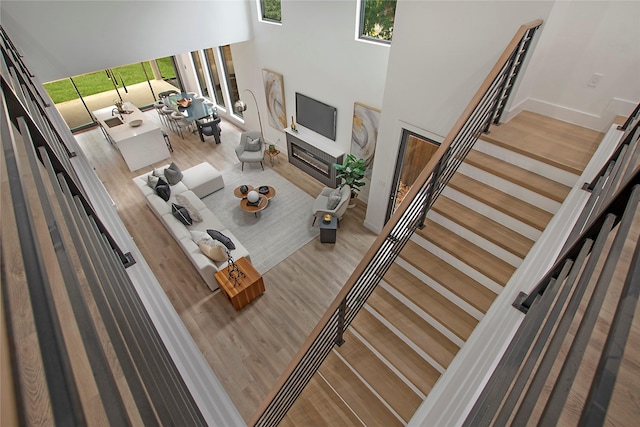 unfurnished living room with a wealth of natural light, a high ceiling, wood finished floors, and a glass covered fireplace