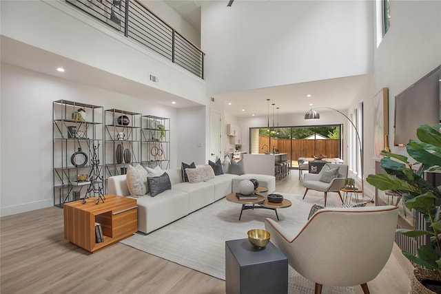 living area with baseboards, visible vents, a high ceiling, and wood finished floors