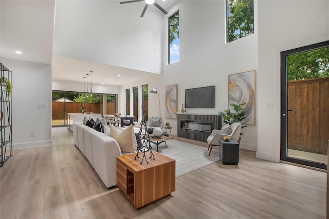 living room with light wood finished floors, baseboards, a towering ceiling, recessed lighting, and a ceiling fan