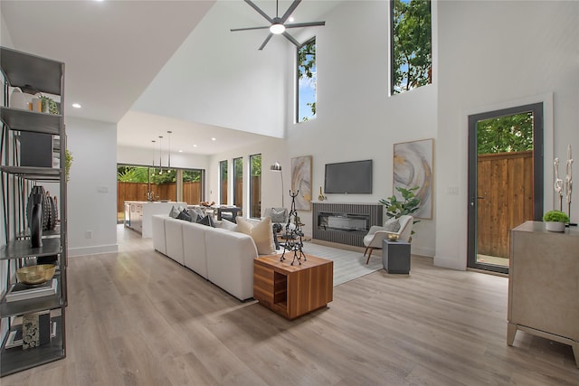 living room featuring baseboards, ceiling fan, light wood-style floors, and a brick fireplace