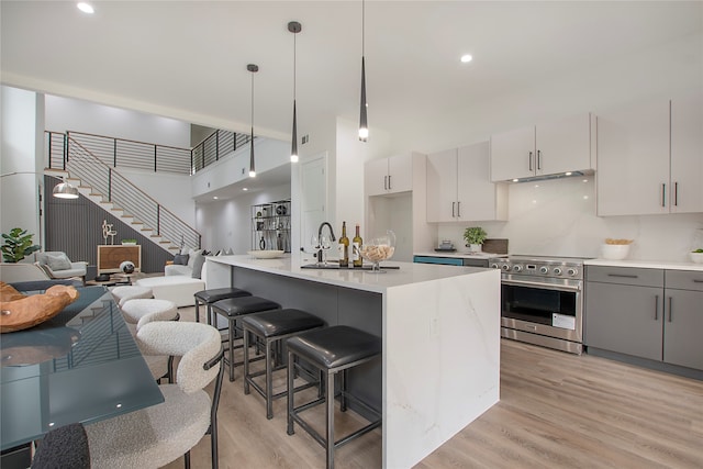 kitchen with decorative light fixtures, light wood-type flooring, a kitchen island with sink, and stainless steel range with electric stovetop