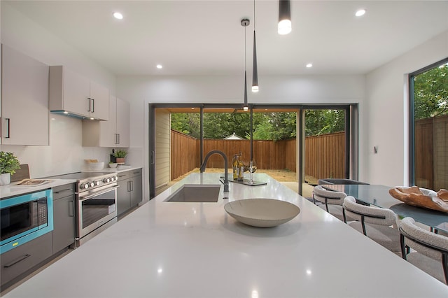 kitchen with stainless steel stove, a sink, built in microwave, decorative light fixtures, and recessed lighting