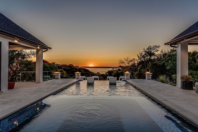 pool at dusk featuring a water view and a patio