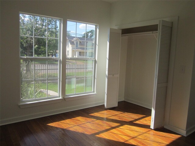 unfurnished bedroom with wood-type flooring, baseboards, a closet, and multiple windows