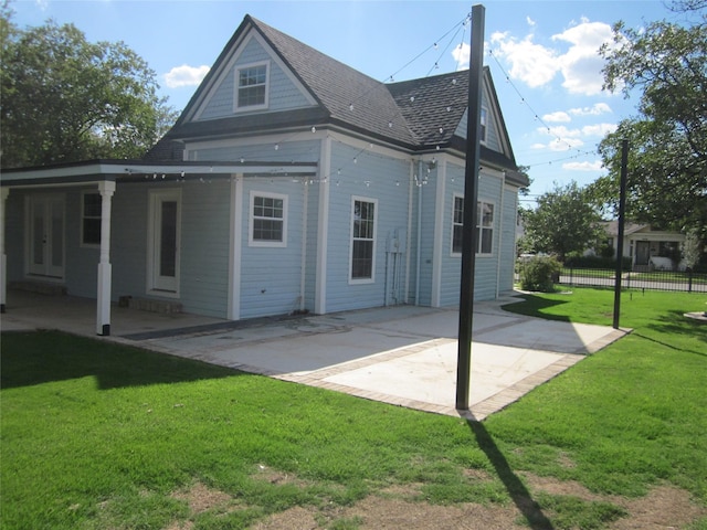 rear view of house featuring a lawn, roof with shingles, fence, and a patio area