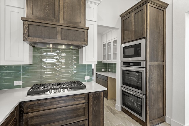 kitchen featuring dark brown cabinetry, decorative backsplash, stainless steel appliances, and custom range hood