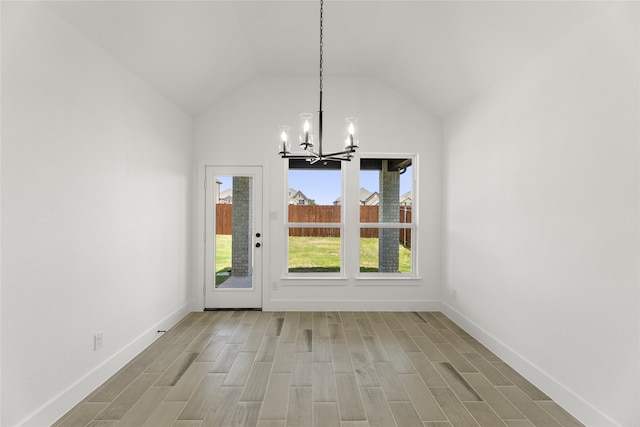 unfurnished dining area with wood-type flooring, an inviting chandelier, and vaulted ceiling