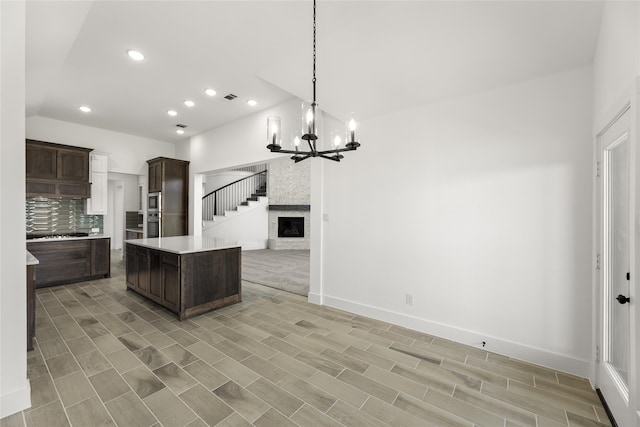 kitchen with dark brown cabinetry, light hardwood / wood-style flooring, a kitchen island, a large fireplace, and decorative light fixtures