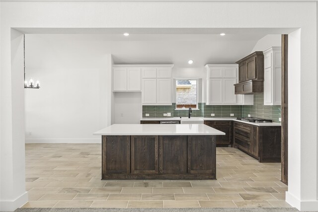 kitchen with stainless steel gas cooktop, white cabinetry, sink, an inviting chandelier, and a center island