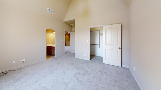 unfurnished bedroom with light carpet, a closet, connected bathroom, and high vaulted ceiling