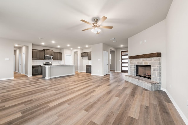 unfurnished living room featuring a stone fireplace, light hardwood / wood-style floors, and ceiling fan