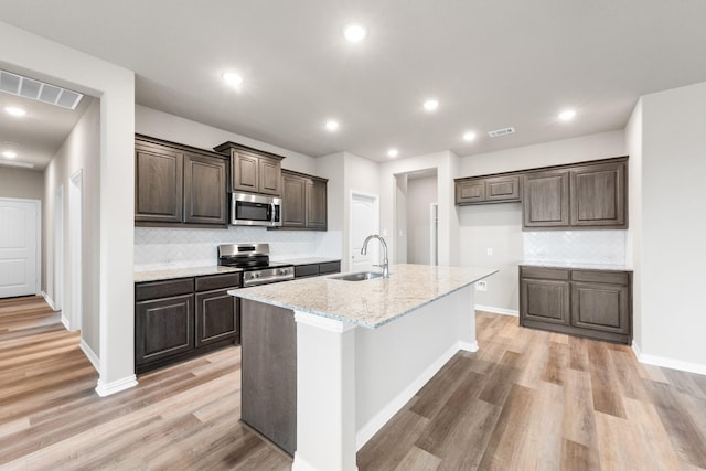 kitchen with sink, an island with sink, stainless steel appliances, light stone countertops, and light hardwood / wood-style floors