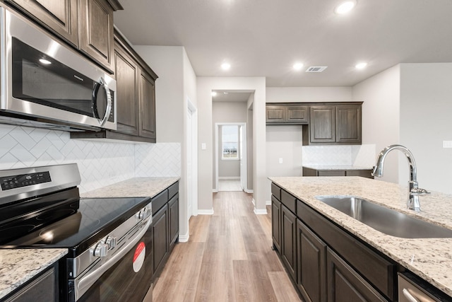 kitchen featuring appliances with stainless steel finishes, sink, dark brown cabinetry, light stone counters, and light wood-type flooring