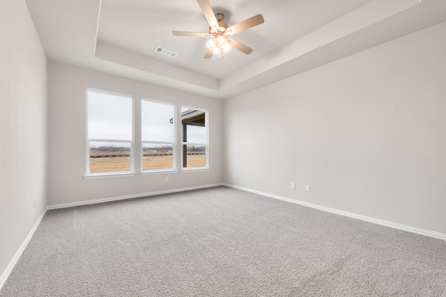 carpeted empty room with ceiling fan and a raised ceiling