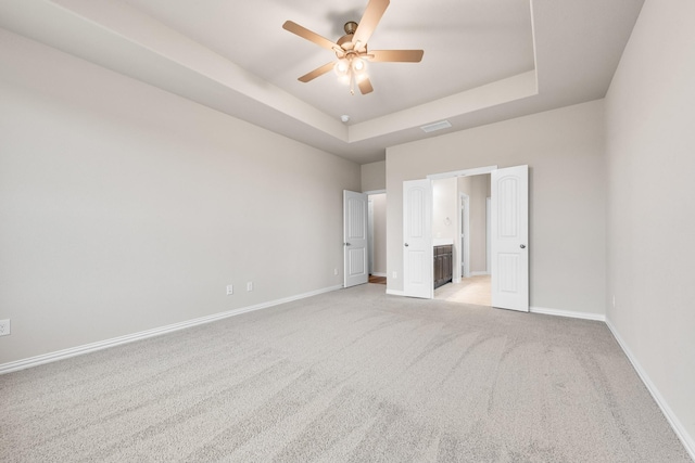 unfurnished bedroom with light carpet, a raised ceiling, ceiling fan, and ensuite bathroom