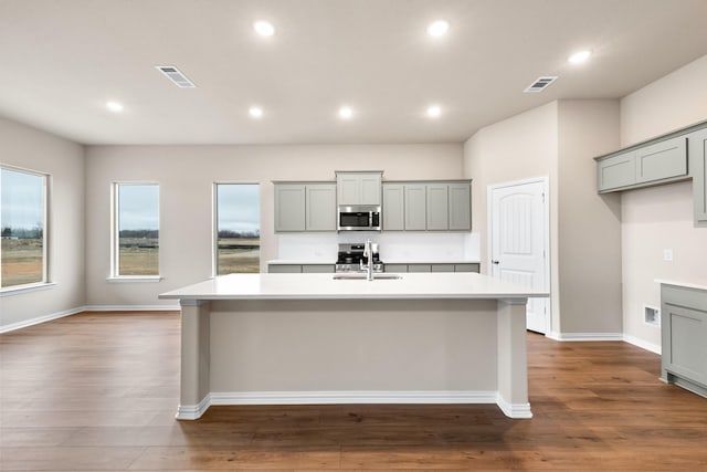 kitchen featuring a kitchen island with sink, stainless steel appliances, and gray cabinetry