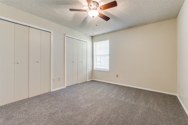 unfurnished bedroom featuring ceiling fan, multiple closets, a textured ceiling, and carpet