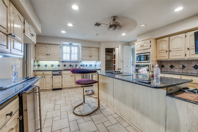 kitchen with dark stone countertops, tasteful backsplash, stainless steel appliances, ceiling fan, and a breakfast bar area