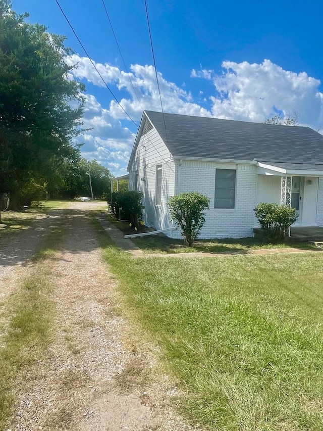 view of property exterior featuring driveway, brick siding, and a yard
