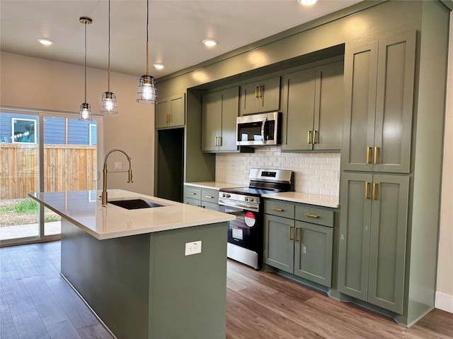 kitchen with appliances with stainless steel finishes, decorative light fixtures, sink, a kitchen island with sink, and green cabinetry