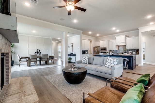 living room with light wood-type flooring, crown molding, a fireplace, and ceiling fan