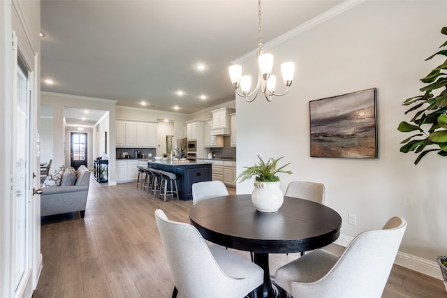 dining room featuring a notable chandelier, light wood-type flooring, sink, and crown molding