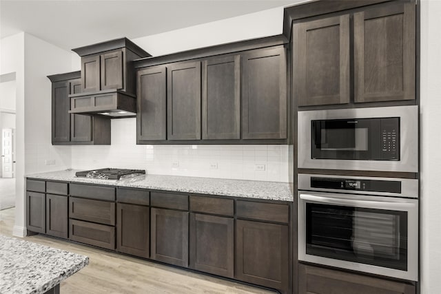 kitchen featuring dark brown cabinets, stainless steel appliances, light stone countertops, light hardwood / wood-style floors, and decorative backsplash