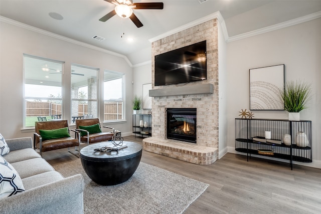 living room with vaulted ceiling, a brick fireplace, wood-type flooring, ceiling fan, and ornamental molding