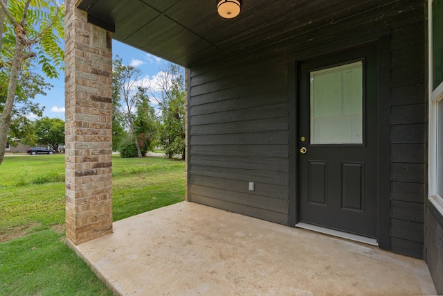 view of exterior entry with a lawn and a patio