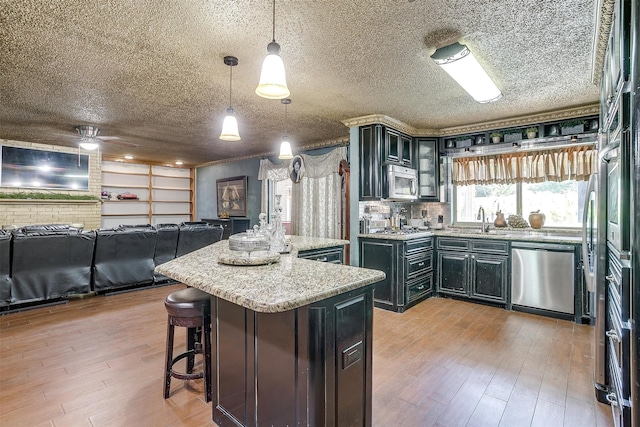 kitchen with light hardwood / wood-style flooring, a kitchen island, sink, hanging light fixtures, and appliances with stainless steel finishes