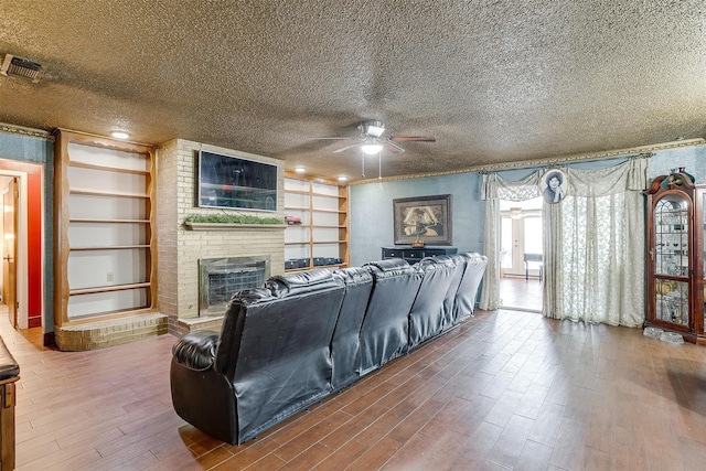 living room with hardwood / wood-style flooring, a textured ceiling, a brick fireplace, and ceiling fan