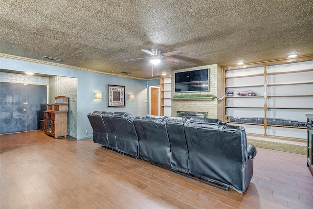 living room with a textured ceiling, wood-type flooring, a brick fireplace, and ceiling fan