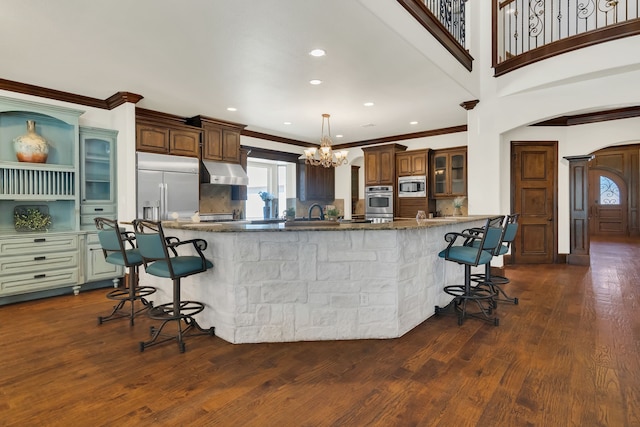 kitchen featuring kitchen peninsula, built in appliances, a breakfast bar, and dark hardwood / wood-style floors