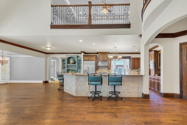 kitchen with light stone countertops, built in appliances, dark wood-type flooring, and a breakfast bar area