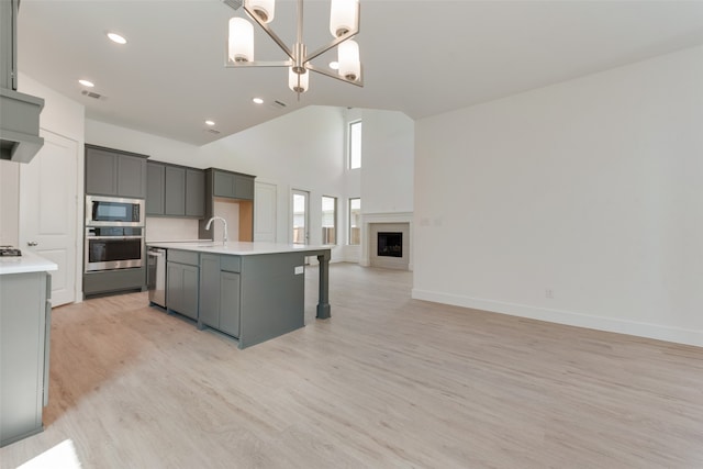 kitchen featuring light hardwood / wood-style floors, stainless steel appliances, a kitchen island with sink, gray cabinets, and pendant lighting