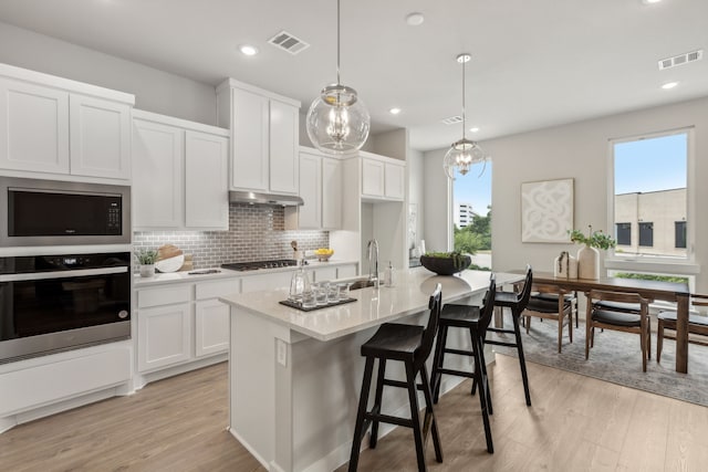 kitchen with stainless steel appliances, a center island with sink, white cabinetry, and a healthy amount of sunlight