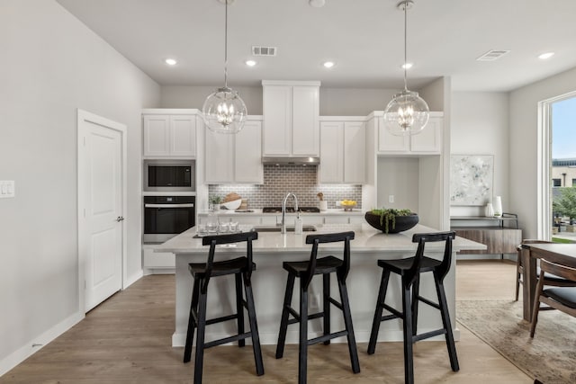 kitchen featuring a kitchen island with sink, a chandelier, appliances with stainless steel finishes, white cabinets, and light hardwood / wood-style floors