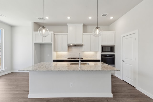 kitchen featuring under cabinet range hood, white cabinetry, black oven, built in microwave, and tasteful backsplash