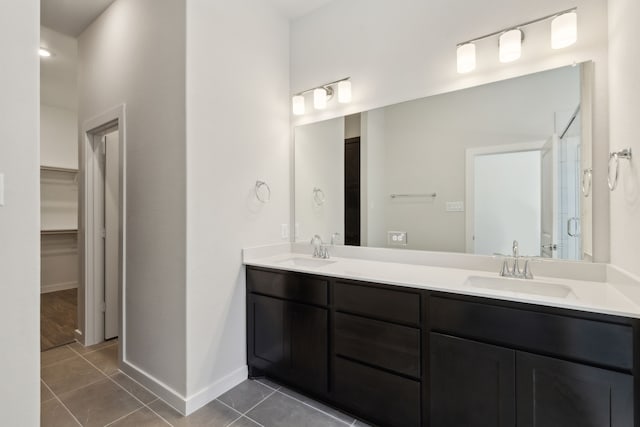 full bath featuring a stall shower, double vanity, a sink, and tile patterned floors