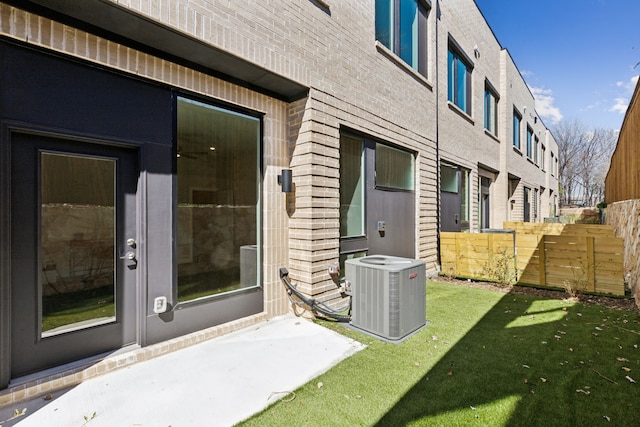 doorway to property featuring a yard, brick siding, fence, and central air condition unit