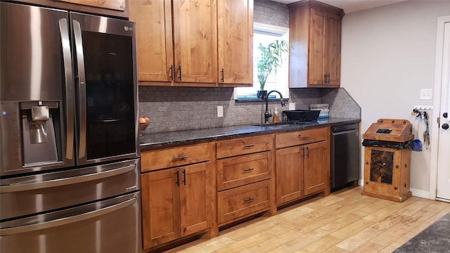 kitchen with sink, black dishwasher, stainless steel fridge with ice dispenser, dark stone counters, and light wood-type flooring