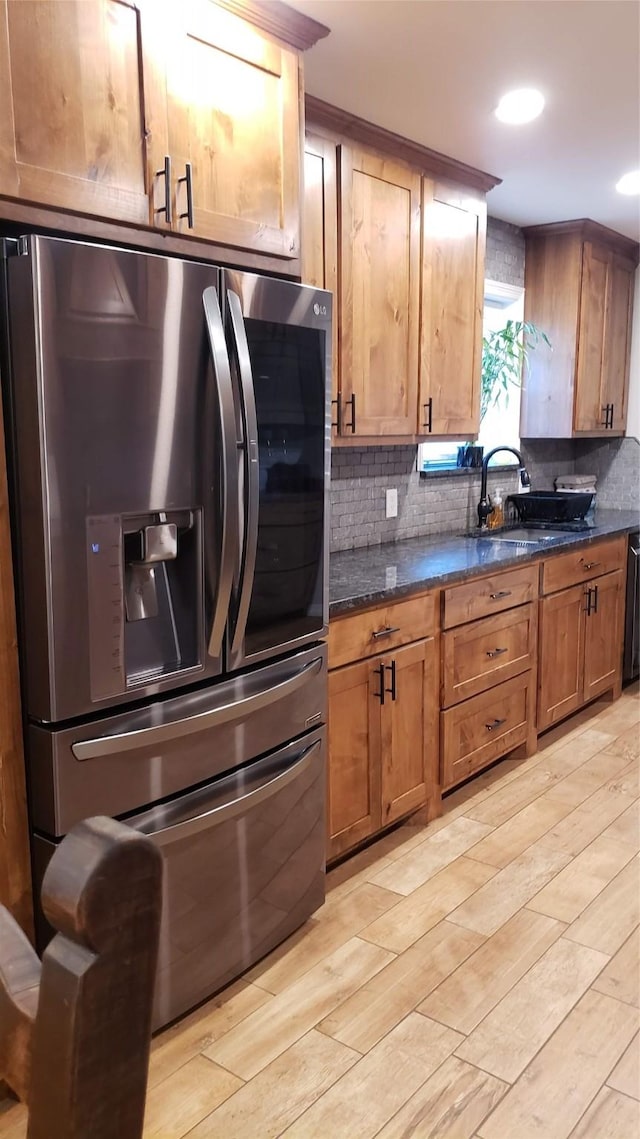 kitchen featuring sink, stainless steel fridge, dark stone countertops, tasteful backsplash, and light wood-type flooring