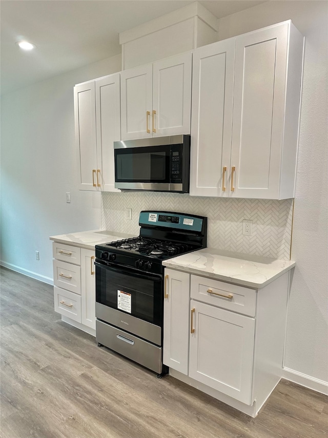 kitchen with backsplash, stainless steel appliances, white cabinets, and light hardwood / wood-style floors