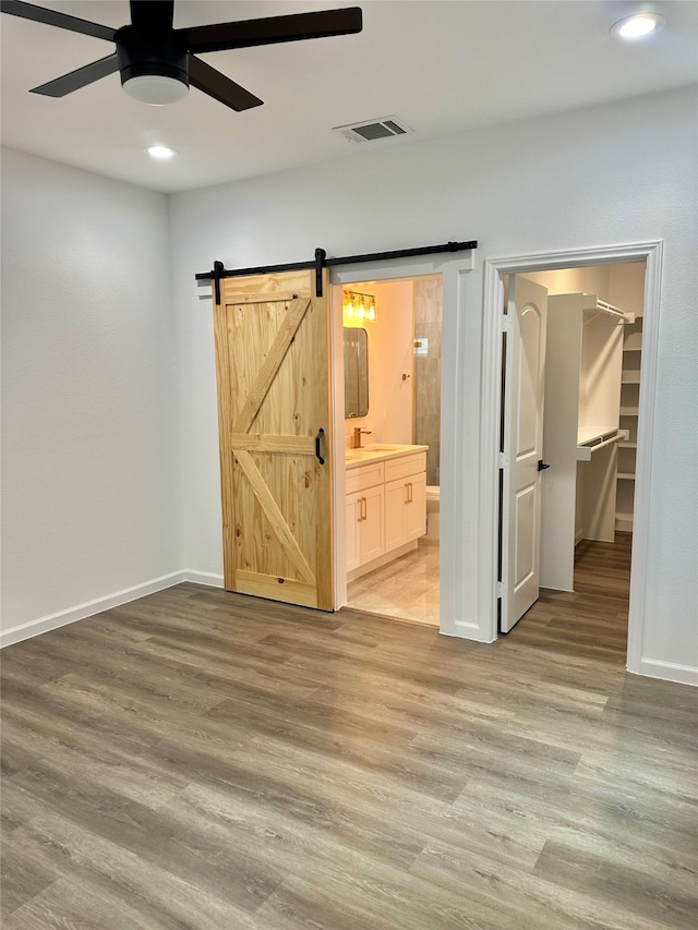 unfurnished bedroom featuring connected bathroom, ceiling fan, a spacious closet, a barn door, and light hardwood / wood-style floors