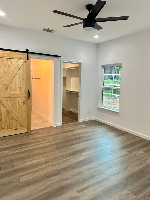 unfurnished bedroom featuring hardwood / wood-style floors, ceiling fan, a closet, a walk in closet, and a barn door