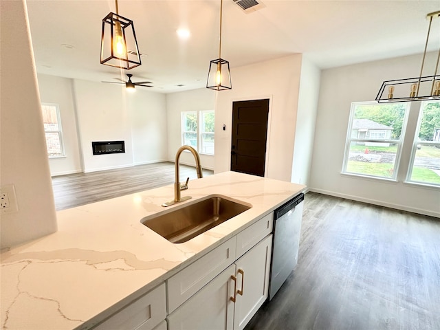 kitchen featuring stainless steel dishwasher, light stone counters, sink, and decorative light fixtures