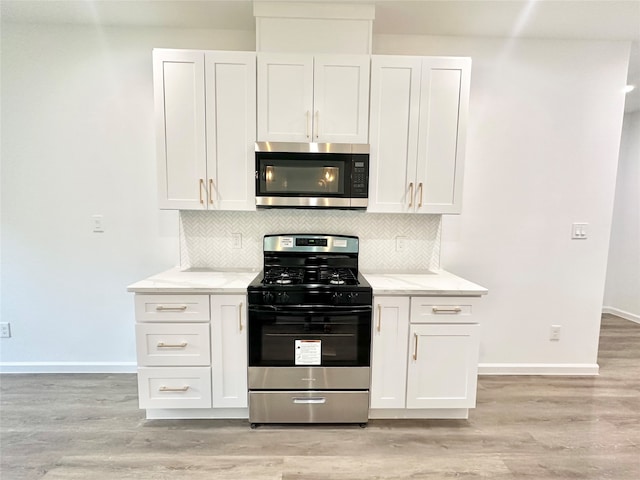 kitchen featuring light wood-type flooring, white cabinetry, light stone counters, decorative backsplash, and appliances with stainless steel finishes