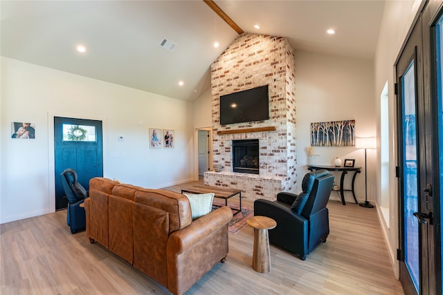 living room with light hardwood / wood-style flooring, high vaulted ceiling, beamed ceiling, and a brick fireplace