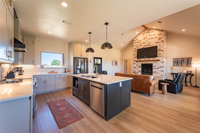 kitchen with a kitchen island with sink, a fireplace, pendant lighting, sink, and appliances with stainless steel finishes