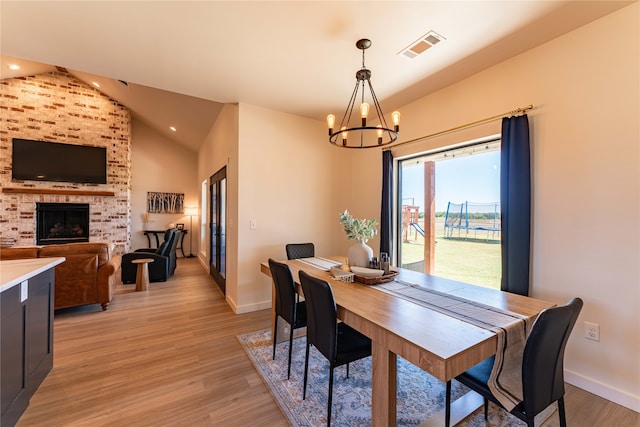 dining area with lofted ceiling, light hardwood / wood-style floors, a notable chandelier, and a brick fireplace